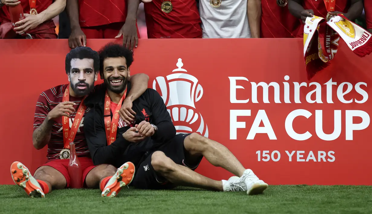 <p>Gelandang Liverpool Thiago mengenakan topeng Mohamed Salah dan meemluk rekannya tersebut setelah mereka memenangkan partai final Piala FA atas Chelsea di Stadion Wembley pada Minggu (16/5/2022) dini hari WIB. Liverpool sukses menjuarai Piala FA 2021/2022 mengalahkan Chelsea lewat adu penalti 6-5. (AP Photo/Ian Walton)</p>