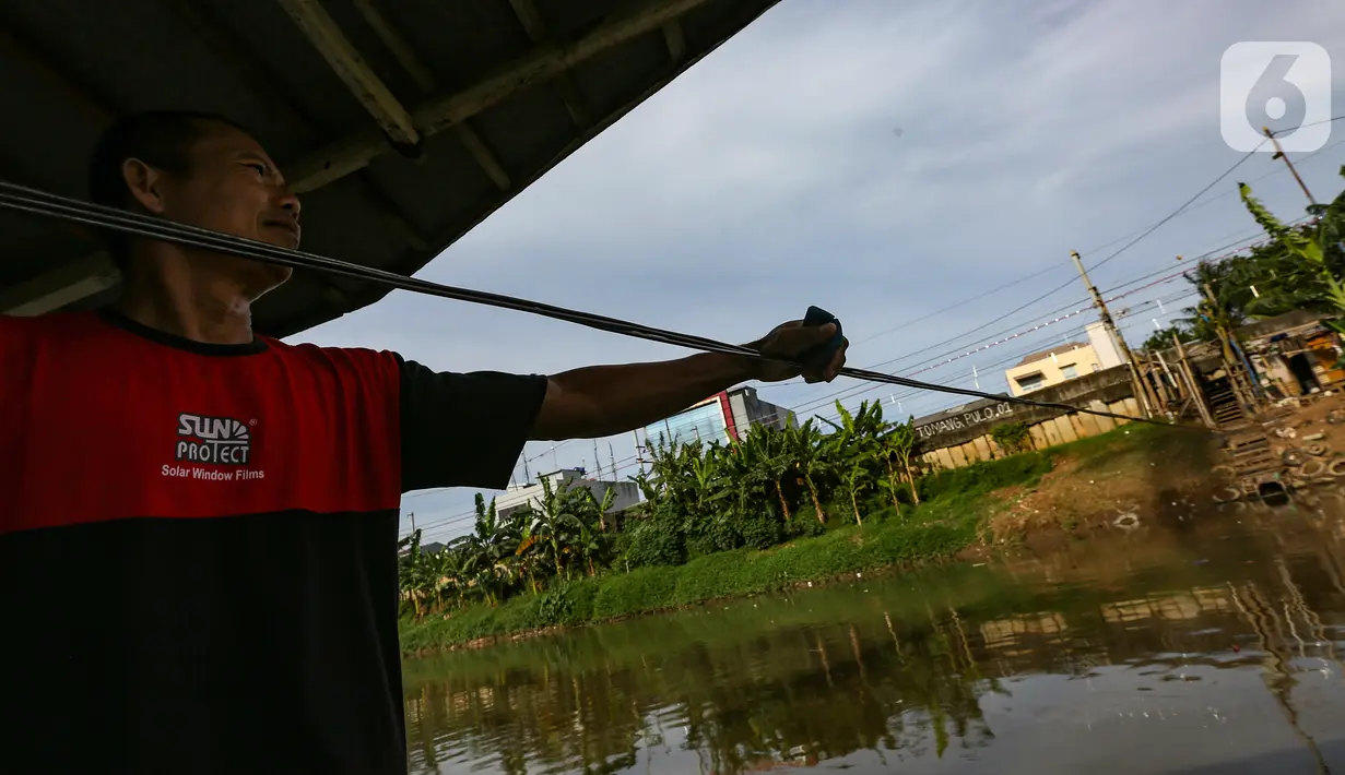 Romli, menarik perahu eretan menggunakan tali baja di Banjir Kanal Barat, Jatipulo, Jakarta, Senin (31/01/2022). Jasa transportasi tradisional, perahu eretan yang beroperasi sejak tahun 1990 hanya dikenakan tarif Rp 2000 sekali menyeberang dari pagi hingga sore hari. (Liputan6.com/Fery Pradolo)