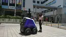 Seorang pejalan kaki berdiri di depan robot yang berpatroli di distrik perbelanjaan dan perumahan selama uji coba di Singapura, Senin (6/9/2021). Pengerahan Xavier akan mendukung pekerjaan petugas publik karena akan mengurangi tenaga yang dibutuhkan untuk patroli jalan kaki. (ROSLAN RAHMAN/AFP)