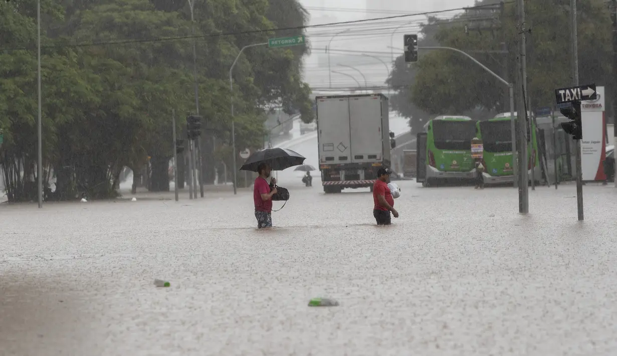 Pejalan kaki menyeberangi jalan yang banjir di Sao Paulo, Brasil, Senin, (10/2/2020). Hujan deras yang membanjiri kota, menyebabkan pinggir sungai utama meluap. (AP Photo/Andre Penner)