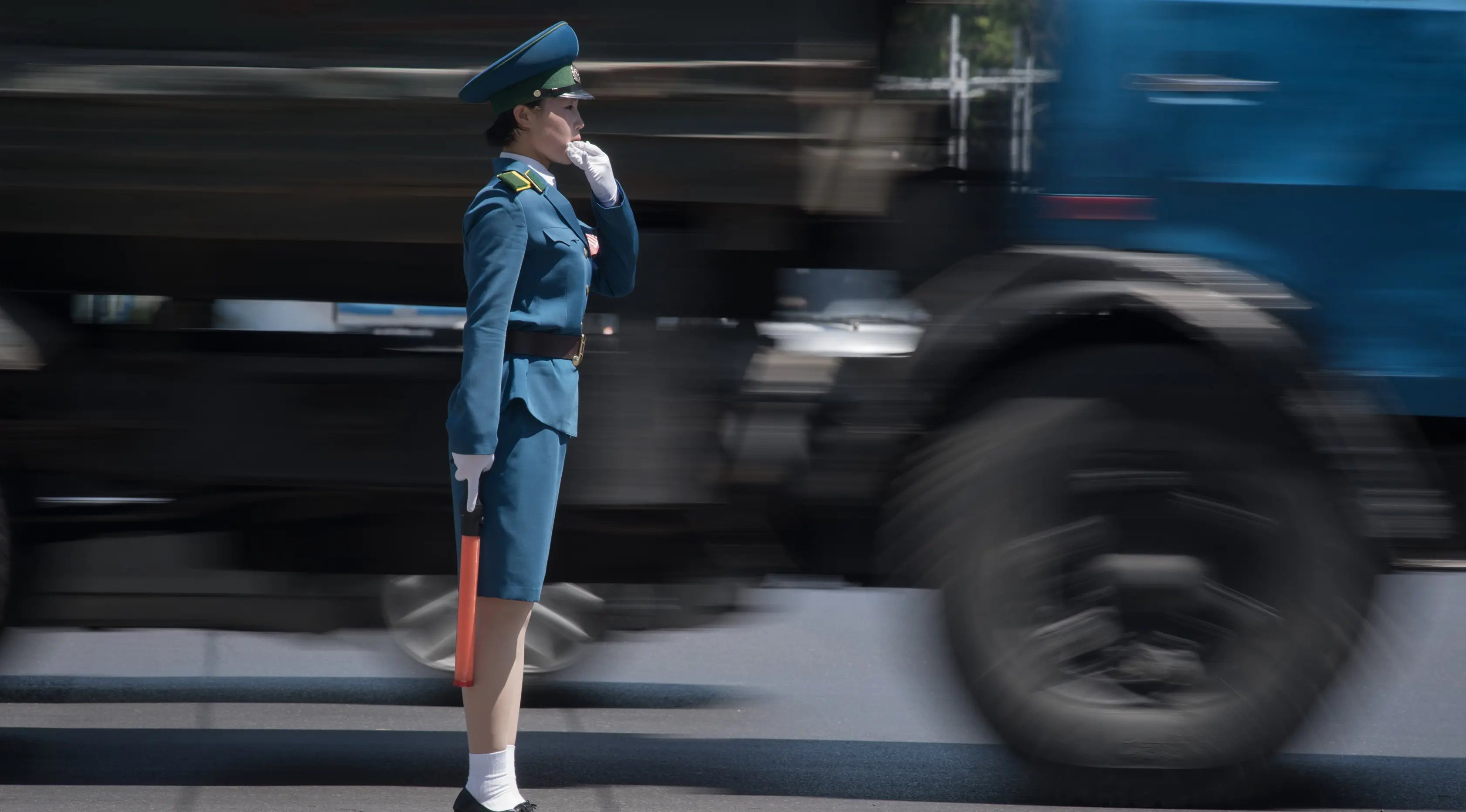 Seorang polisi wanita mengatur lalu lintas di sebelah truk yang melintas di Pyongyang, Korea Utara (5/6). Para polisi wanita ini harus meninggalkan profesi mereka jika mereka menikah dan akan pensiun ketika memasuki usia 26 tahun. (AFP Photo/Ed Jones)