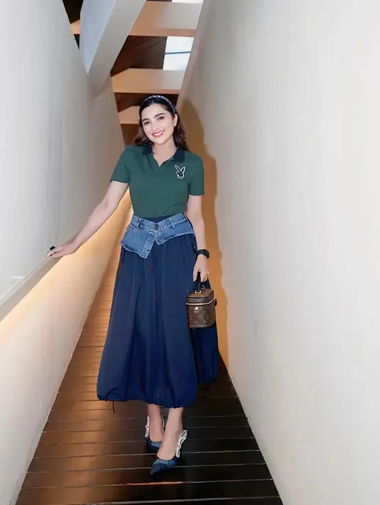 Ia tampil dalam balutan atasan hijau gelap dengan detail minimalis yang dipadukan dengan rok midi denim. Sentuhan unik terlihat dari aksen denim yang membingkai pinggangnya, memberikan kesan modern sekaligus santai. Rambutnya yang tertata rapi dengan headband menambahkan nuansa feminin pada penampilannya. [@ashanty_ash].