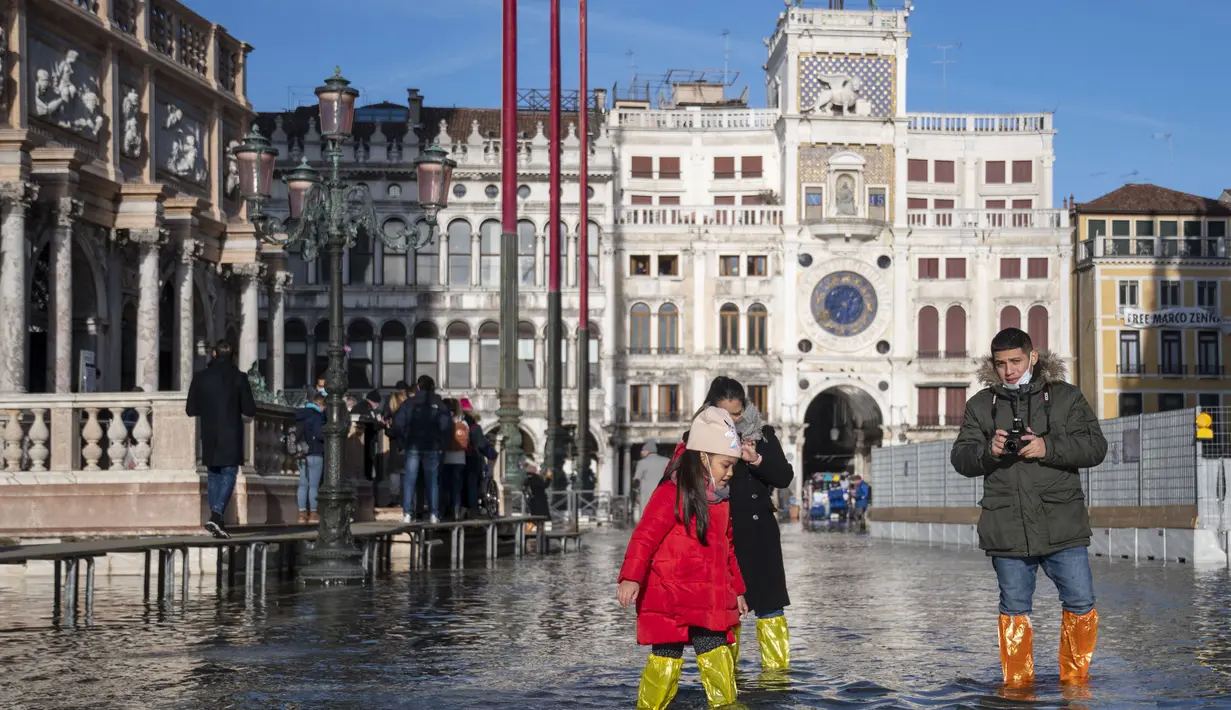 Orang menggunakan jembatan trestle untuk menyeberangi St Mark's Square yang dibanjiri air laut, di Venesia, Italia, Sabtu (4/12/2021). Air mencapai 99 sentimeter di atas permukaan laut dan bagian terendah kota tenggelam. (AP Photo/Luigi Costantini)