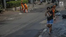 Warga menutupi matanya untuk menghindari sisa gas air mata pasca bentrok massa dengan aparat di Palmerah, Jakarta, Kamis (26/9/2019). Banyak masyarakat yang melintas dan warga sekitar perih pada mata hingga bersin akibat sisa gas air mata pasca bentrokan kemarin. (Liputan6.com/Faizal Fanani)