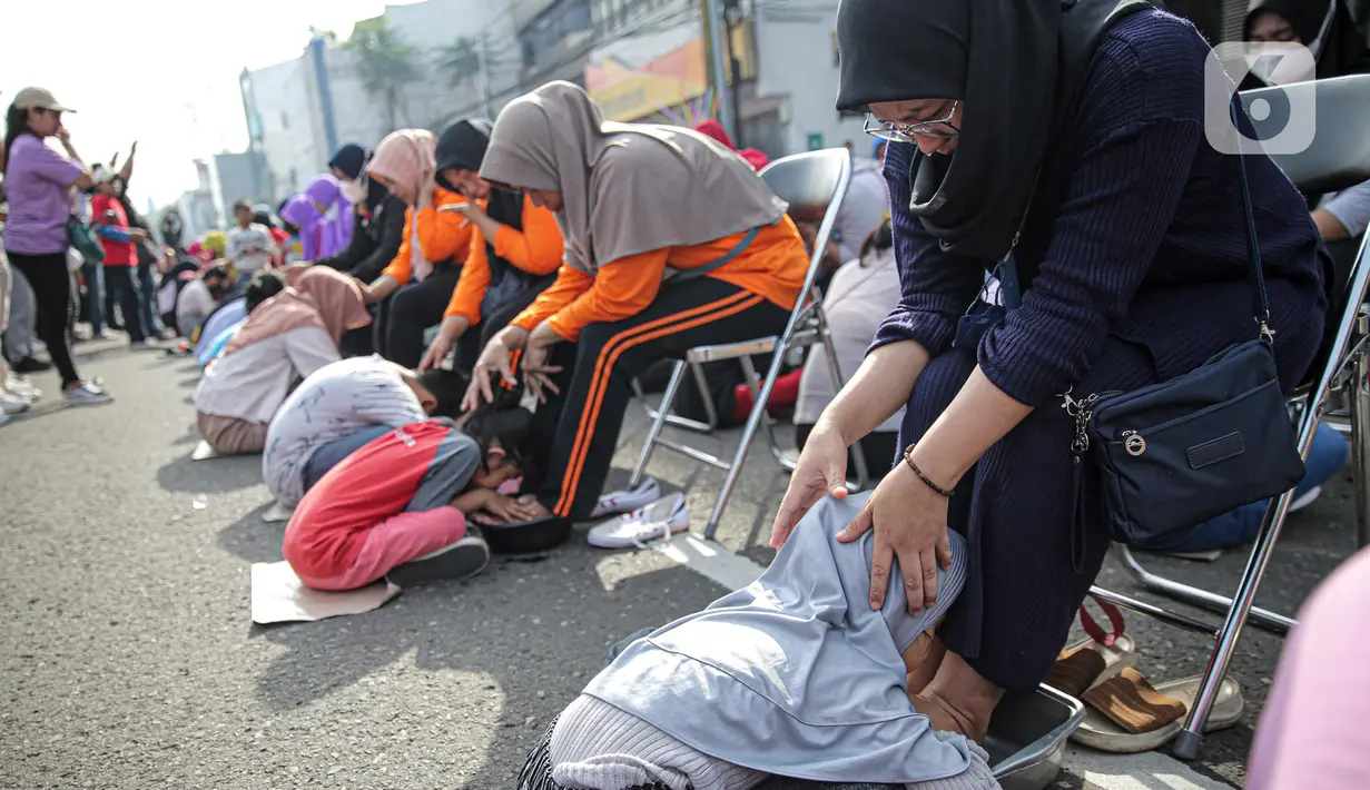 Sejumlah anak mencium kaki ibunya pada aksi cuci kaki ibu massal di Jakarta, Minggu (18/12/2022). Aksi yang diikuti sebanyak ratusann peserta itu bertujuan untuk meningkatkan rasa cinta kasih kepada ibu , khususnya dalam rangka memperingati Hari Ibu. (Liputan6.com/Faizal Fanani)