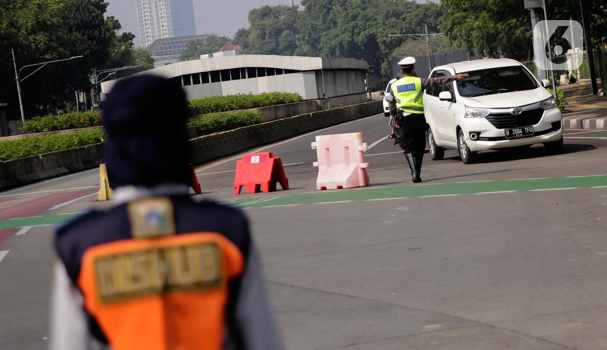 Petugas polisi mengarahkan kendaraan berplat nomor genap di pos penyekatan ganjil-genap di Bundaran Senayan, Minggu (5/9/2021). Pembatasan kendaraan dengan sistem pelat nomor kendaraan ini tetap berlaku di akhir pekan, Sabtu dan Minggu. (Liputan6.com/Angga Yuniar)