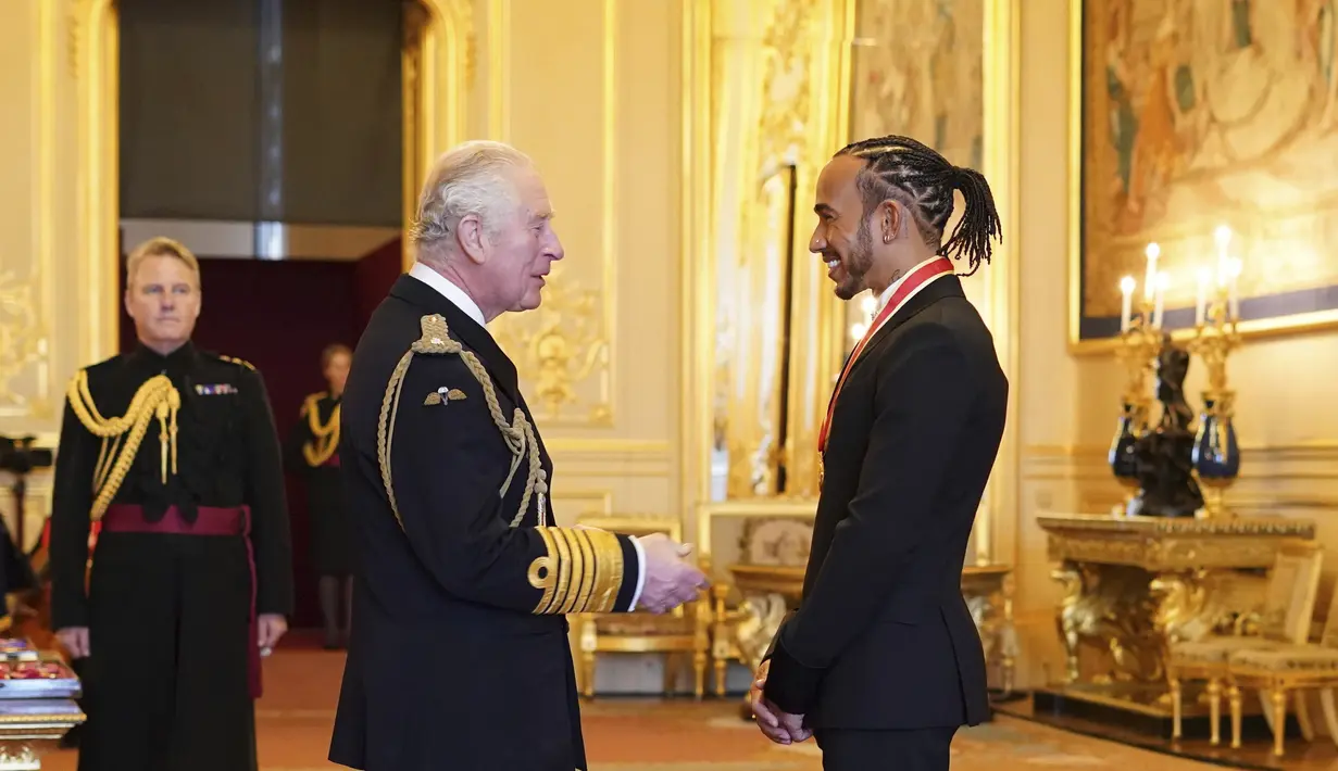 Pembalap Lewis Hamilton berbincang dengan Pangeran Charles setelah menerima gelar kebangsawanan dari Kerajaan Inggris di Kastil Windsor, Rabu (15/12/2021). (Dominic Lipinski/PA via AP)