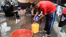 Pengungsi mengisi jerigen dengan air yang dikumpulkan dari tetesan air hujan yang jatuh ke dalam baskom, Jalur Gaza Selatan pada 14 November 2023 (SAID KHATIB/AFP)