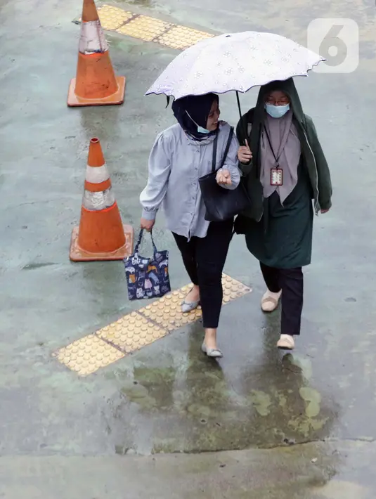 Pekerja menggunakan payung saat melintasi ruas jalan di kawasan Kuningan, Jakarta, Kamis (18/12/2021). BMKG memprakirakan potensi hujan lebat yang mungkin disertai petir dan angin kencang hingga 21 Februari di beberapa provinsi di Indonesia, termasuk DKI Jakarta. (Liputan6.com/Helmi Fithriansyah)