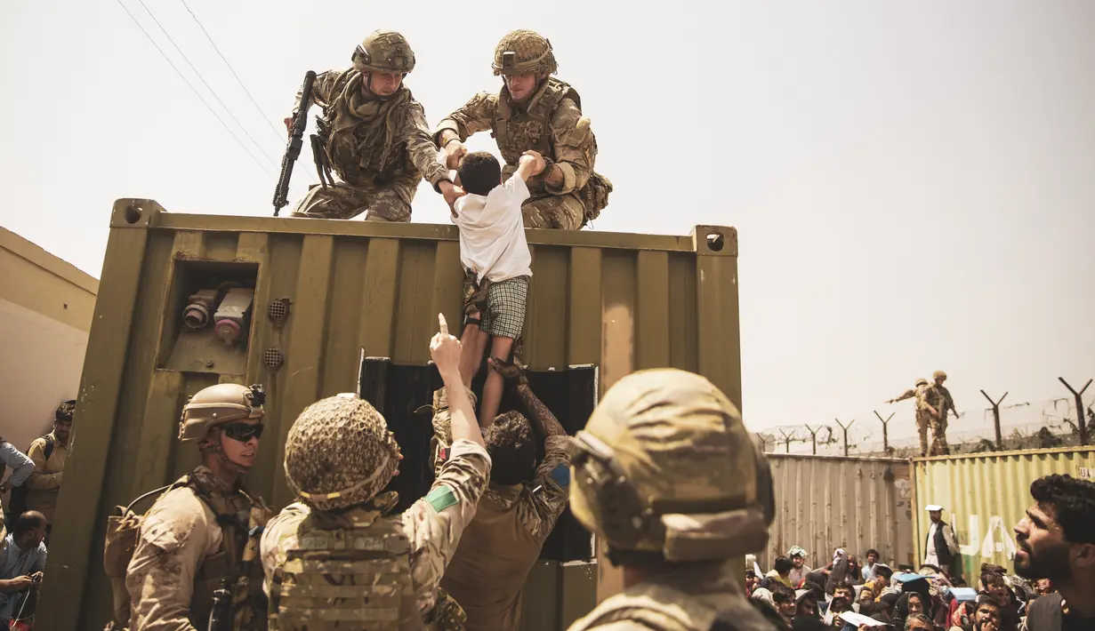 Pasukan koalisi Inggris dan Turki, bersama dengan Marinir AS, membantu seorang anak selama evakuasi di Bandara Internasional Hamid Karzai di Kabul, Afghanistan, Jumat (20/8/2021).  (Staff Sgt. Victor Mancilla/U.S. Marine Corps via AP)