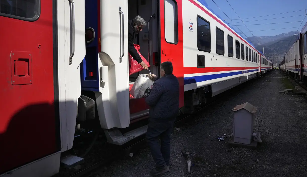 Seorang pria memberikan perbekalan kepada seorang lainnya yang berada di dalam kereta, yang digunakan sebagai tempat berlindung, di kota Iskenderun, Turki selatan, Selasa (14/2/2023). Korban tewas gempa Turki dan Suriah telah menembus 41 ribu jiwa. Masifnya korban tewas ini membuat gempa Turki disebut sebagai "bencana alam terburuk" dalam satu abad terakhir di Eropa. (AP Photo/Hussein Malla)