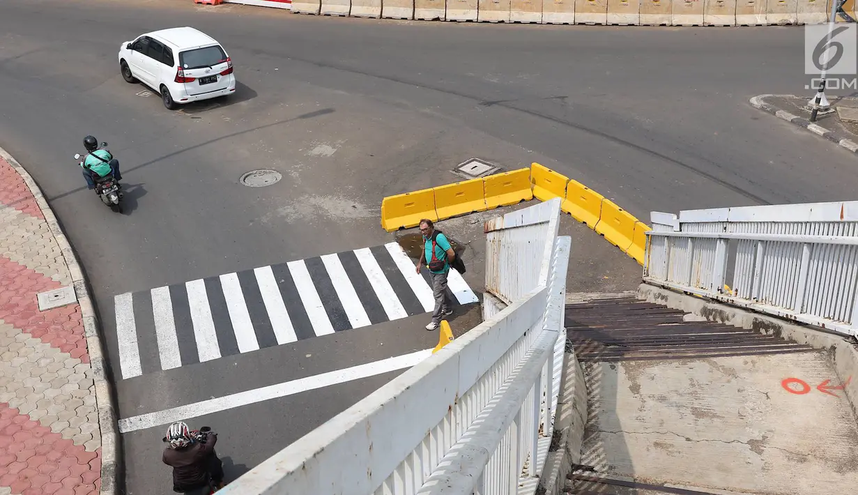 Pejalan kaki melintas di dekat tangga JPO yang berada di tengah jalan Dewi Sartika, Jakarta, Rabu (9/1). Adanya proyek pelebaran jalan menyebabkan posisi trotoar bergeser sehingga tangga JPO menjadi di tengah jalan. (Liputan6.com/Immanuel Antonius)