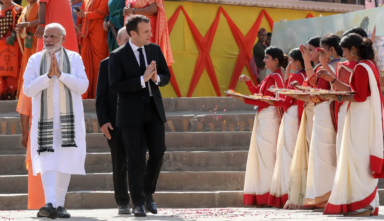 Presiden Prancis Emmanuel Macron (tengah) dan PM India Narendra Modi (kiri) berjalan bersama di Varanasi, India, Senin (12/3). Kunjungan Macron ke India di untuk meneken kesepakatan pertahanan, keamanan, dan energi nuklir. (AFP PHOTO/POOL/Ludovic MARIN)