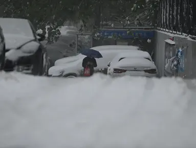 Seorang pria melintas di jalan saat salju turun di Beijing, China, Minggu (7/11/2021). Badai salju awal musim telah menyelimuti sebagian besar Cina utara termasuk ibu kota Beijing, mendorong penutupan jalan dan pembatalan penerbangan. (Noel Celis / AFP)