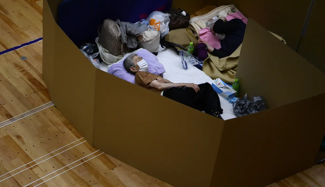 Penduduk setempat beristirahat di pusat evakuasi dengan kotak kardus untuk menjaga jarak di sebuah gimnasium kota Yatsushiro di prefektur Kumamoto, Jepang, Senin (6/7/2020). Hujan deras menghambat operasi pencarian dan penyelamatan korban banjir dan tanah longsor di Kumamoto. (Charly TRIBALLEAU/AFP)