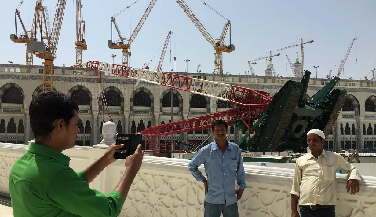 Umat muslim foto bersama dengan latar berlakang crane yang roboh di Masjidil  Haram, Kota Mekah,  Arab Saudi (9/12/2015). Sebanyak 107 calon jemaah haji meninggal dunia akibat crane jatuh karena cuaca buruk. (REUTERS / Mohamed Al Hwaity)