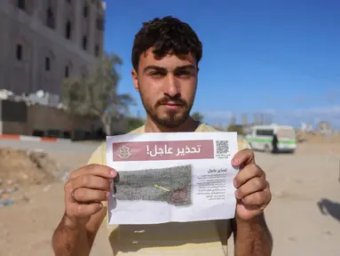 Seorang pria Palestina menunjukkan salah satu selebaran yang disebarkan oleh tentara Israel di Beit Hanun, Jalur Gaza utara pada 19 Maret 2025. (BASHAR TALEB/AFP)