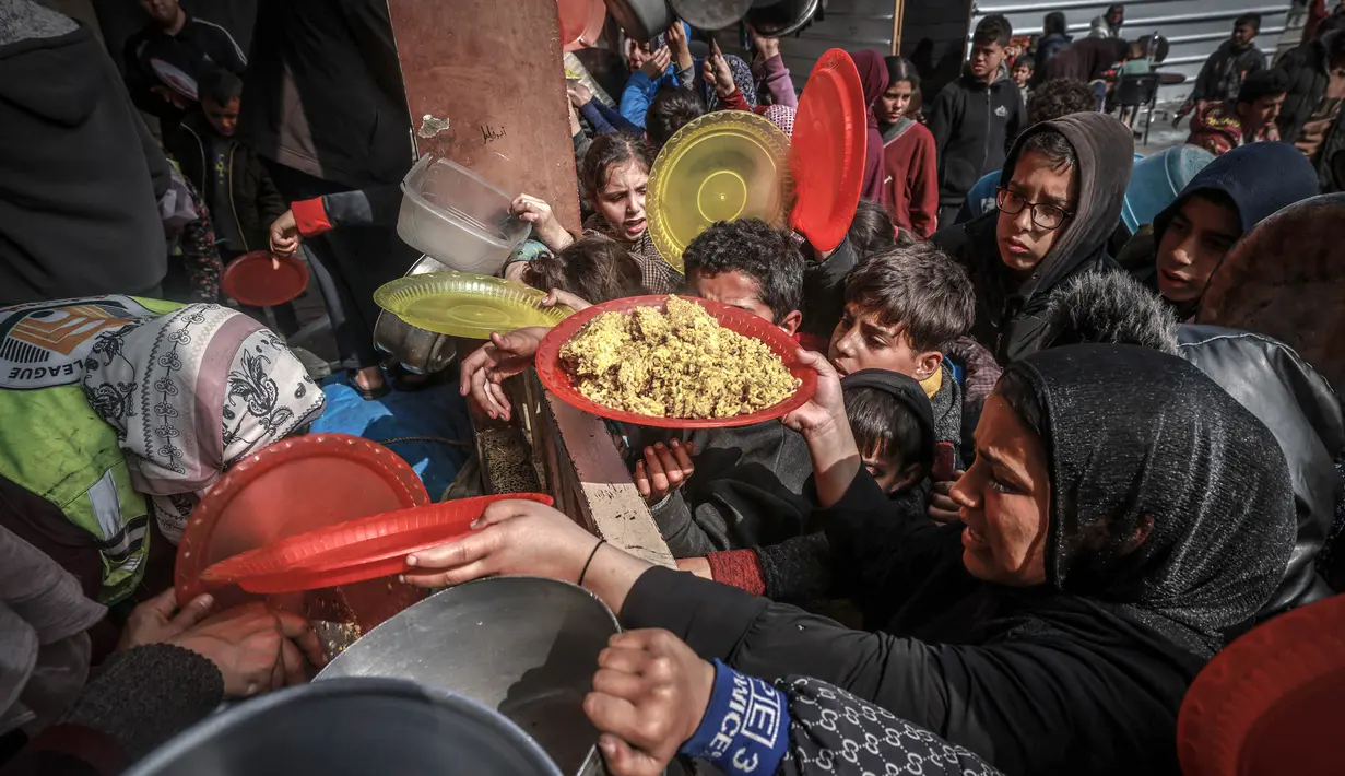 Warga Palestina yang mengungsi berkumpul untuk menerima makanan di sebuah sekolah pemerintah di Rafah di Jalur Gaza selatan pada 19 Februari 2024. (MOHAMMED ABED/AFP)
