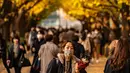 Seorang perempuan membawa anjingnya sambil berjalan di bawah pohon ginkgo dalam warna musim gugur di Taman Luar Kuil Meiji di Tokyo, Kamis (18/11/2021). Pada pertengahan bulan November, barisan pohon ginkgo yang ada di taman ini akan berubah warna menjadi kuning keemasan. (Philip FONG / AFP)