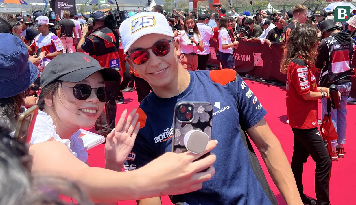 Sorang penggemar melakukan swafoto bersama pembalap CryptoDATA Aprilia RNF, Raul Fernandez, dalam kegiatan MotoGP Hero Walk di Sirkuit Mandalika, Lombok , Minggu (15/10/2023). (Bola.com/Benediktus Gerendo Pradigdo)