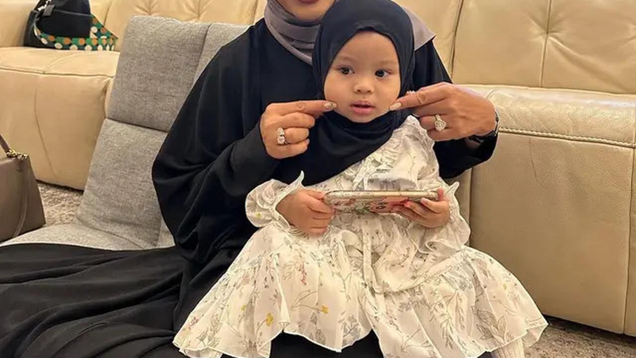 Krisdayanti memangku Ameena yang menggemaskan, dengan dress putih dan hijab hitam.