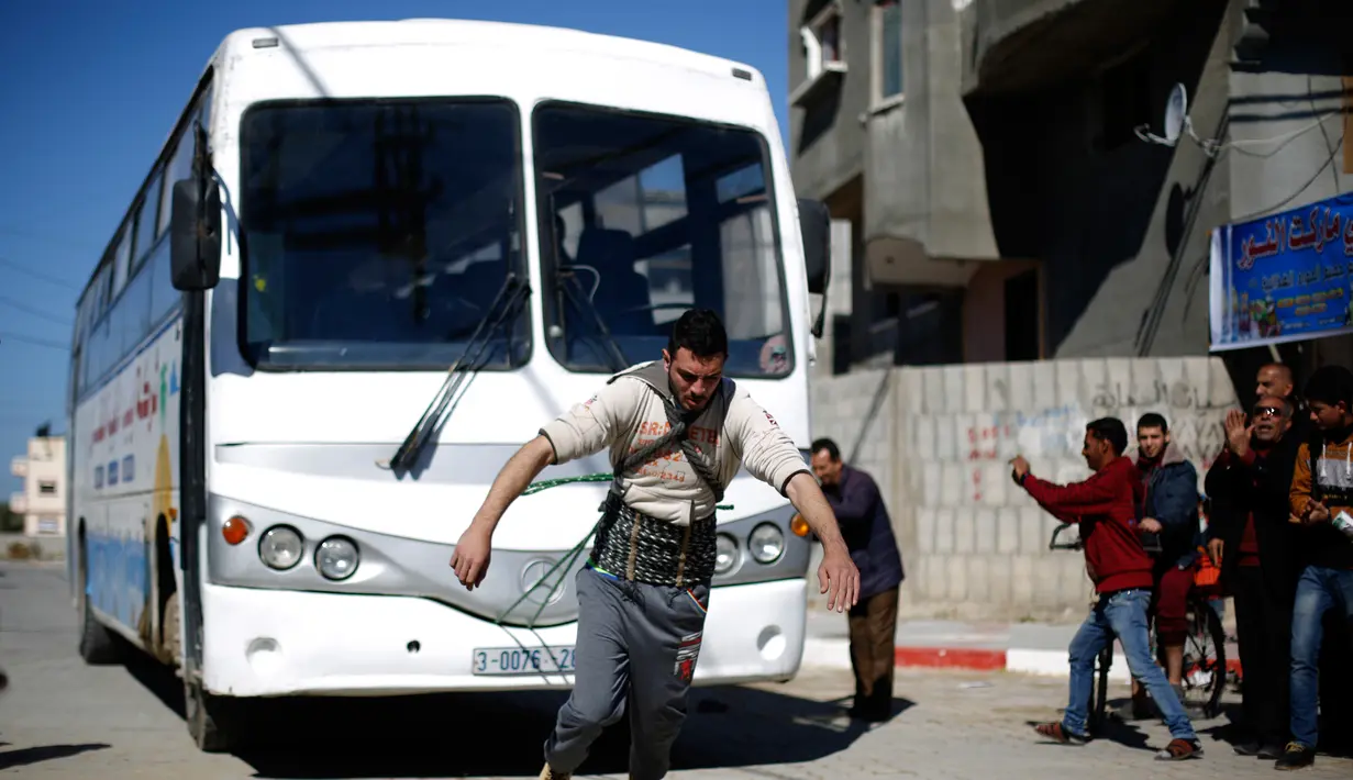Mohamed Barka, pria yang dijuluki "Super Hero" asal Palestina menarik sebuah bus dengan tali yang terikat di tubuh dalam aksinya di Deir Al-Balah, Gaza Tengah, Kamis (4/2). (MOHAMMED ABED/AFP)