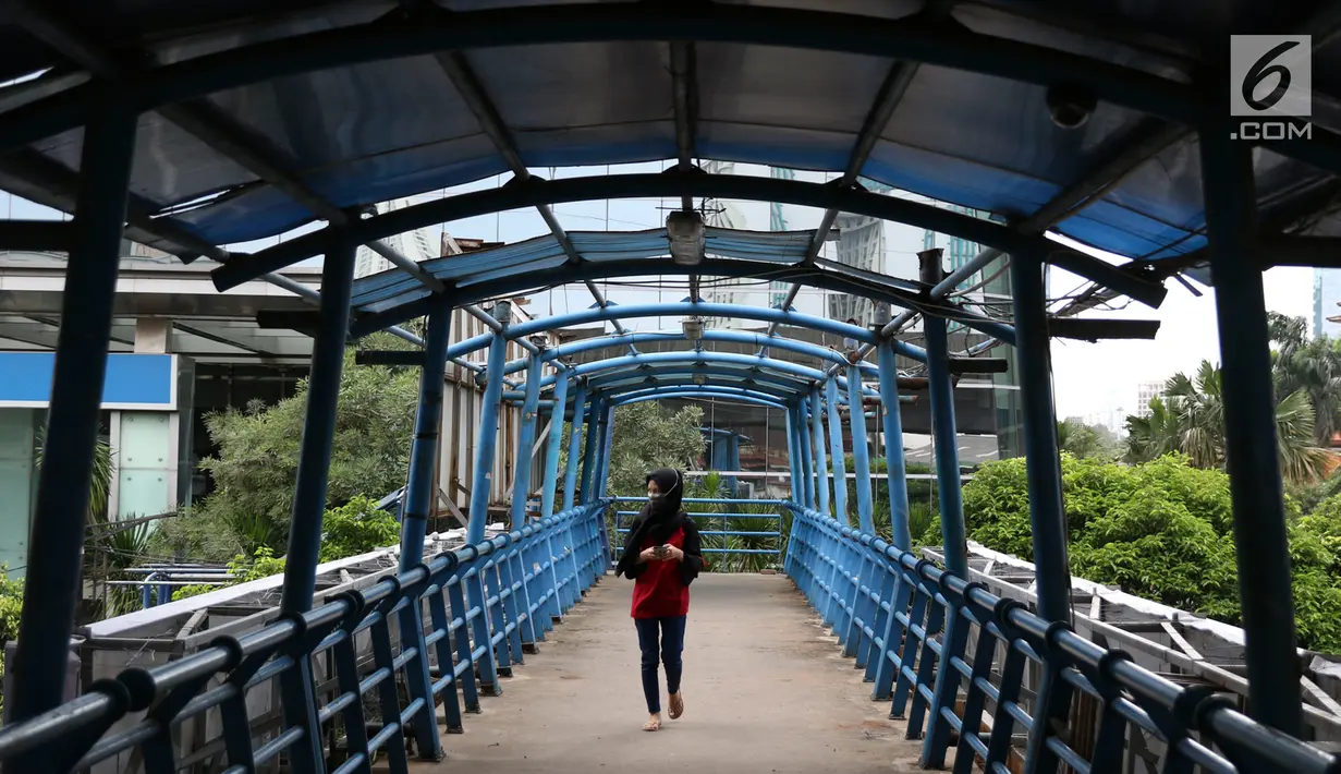Pejalan kaki melintasi JPO yang atapnya rusak di kawasan Kuningan, Jakarta, Minggu (10/2). Kondisi JPO yang sebagian atapnya hilang tersebut mengganggu kenyamanan pejalan kaki, terutama saat hujan. (Liputan6.com/Immanuel Antonius)