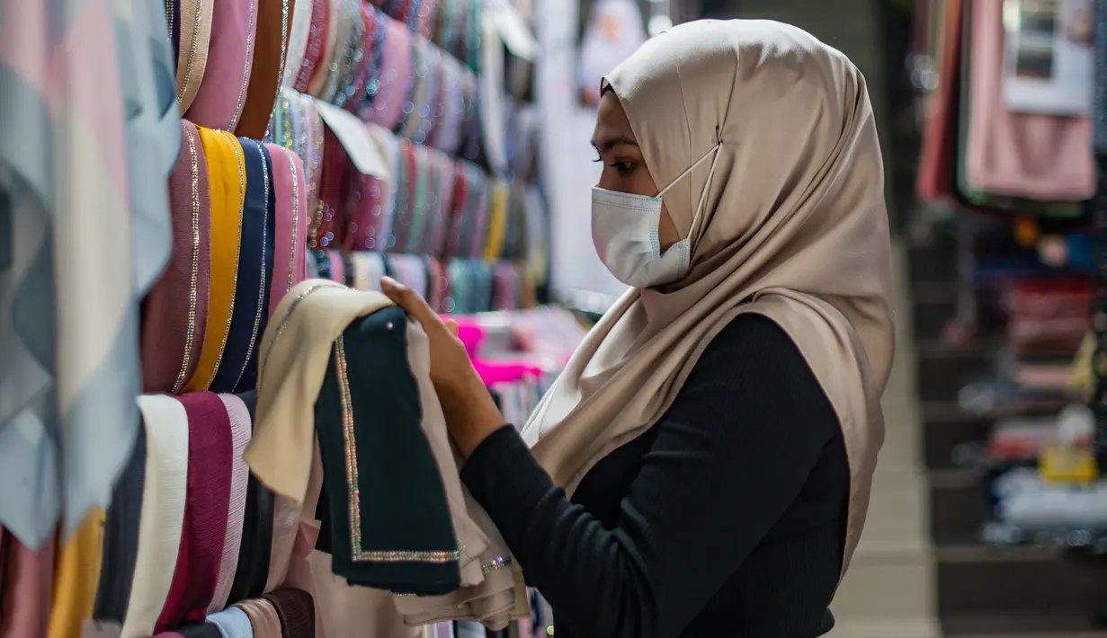 Pekerja mengenakan masker sebagai tindakan pencegahan penyebaran Covid-19 merapikan kerudung menjelang Idul Fitri yang menandai berakhirnya bulan suci Ramadan di Kuala Lumpur (13/5/2020). (AFP/Mohd Rasfan)