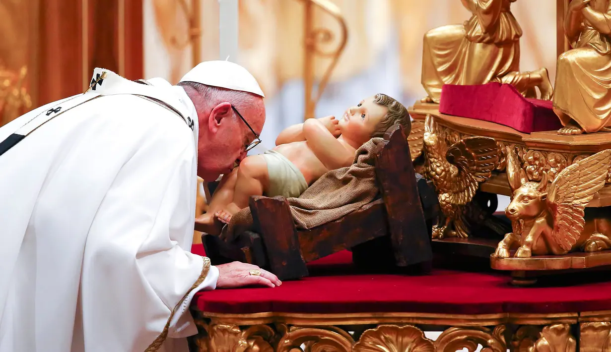 Paus Fransiskus mencium patung bayi Yesus saat memimpin misa Natal di Basilika Santo Petrus, Vatikan, (24/12).  Pada misa tersebut, Paus mengatakan bahwa Natal sudah "disandera" oleh materialisme. (REUTERS/Tony Gentile)