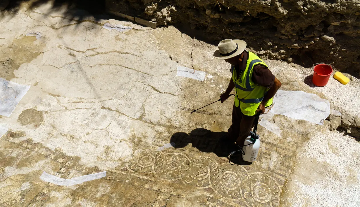 Seorang Arkeolog membersihkan pasir-pasir yang menutupi mosaik menggunakan air di Larnaca, Siprus (14/7).Mereka percaya bahwa mosaik ini merupakan peninggalan Romawi dari Kerajaan Kition. (Iakovos Hatzistavrou / AFP)