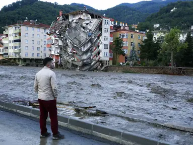 Seorang pria melihat saat air banjir menyapu di kota Bozkurt, provinsi Kastamonu, Turki, Kamis (12/8/2021). Banjir yang dipicu oleh hujan lebat melanda provinsi pesisir Laut Hitam Bartin, Kastamonu, Sinop dan Samsun. (IHA via AP)