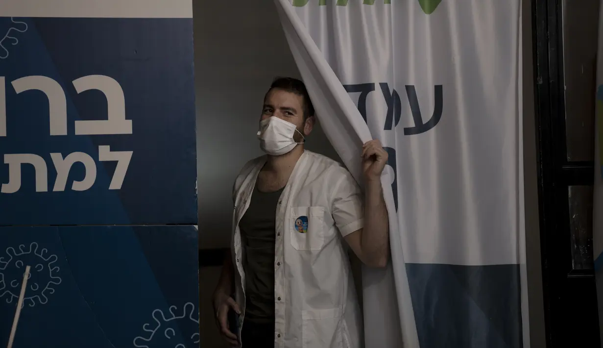 Pekerja medis Clalit Health Services mengintip dari stannya saat memanggil pasien berikutnya untuk divaksin covid-19 di Yerusalem, Senin (3/1/2022). Israel menyetujui pemberian dosis booster tersebut kepada kelompok warga berusia di atas 60 tahun dan tenaga medis. (AP Photo/Maya Alleruzzo)