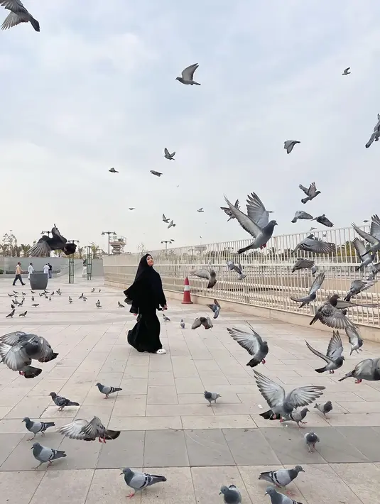 Mengabadikan foto bersama burung-burung di sekitaran Tanah Suci, Fuji terlihat mengenakan gamis dan hijab syar’i hitam. [Instagram/@fuji_an]