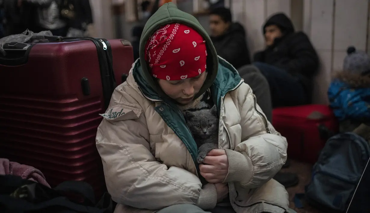 Seorang gadis Ukraina memelihara kucingnya dengan mantelnya di dalam stasiun kereta api Lviv, 28 Februari 2022, di Lviv, Ukraina barat. Dalam eksodus lebih dari 2,5 juta orang yang melarikan diri dari invasi Rusia, terdapat hewan peliharaan yang tidak dapat ditinggalkan. (AP Photo/Bernat Armangue)