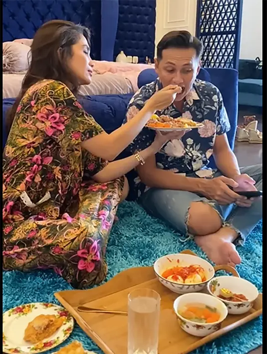 Ussy dengan mengenakan daster suapi suami yang menikahinya sejak tahun 2012 silam. Dalam salah satu kanal Youtubenya, Ussy mengaku cara membuat sang suami agar ketergantungan adalah memberikan perhatian khusus, salah satunya menyuapi. [Youtube/Ussy Andhika Official]