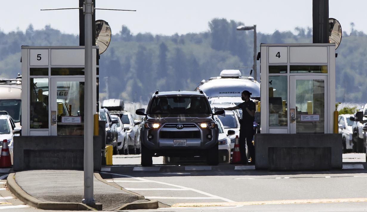 Petugas Badan Layanan Perbatasan Kanada menyerahkan dokumen ke pengendara yang memasuki Kanada di perbatasan Douglas-Peace Arch, Surrey, British Columbia, Kanada, Senin (9/8/2021). Kanada mencabut larangan terhadap warga AS melintasi perbatasaan negaranya. (Darryl Dyck/The Canadian Press via AP)