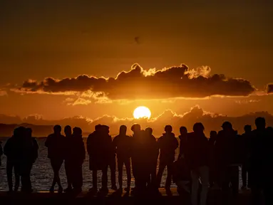Orang-orang berkumpul di Pantai Selatan Chigasaki untuk menyaksikan matahari terbit pada Hari Tahun Baru di Prefektur Kanagawa, barat daya Tokyo (1/1/2021). Berburu matahari terbit di awal tahun tentu bisa menjadi salah satu aktivitas seru saat merayakan pergantian tahun. (AFP/Philip Fong)