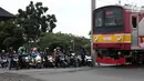 Pengendara sepeda motor menghentikan kendaraannya saat sebuah kereta api melintas di perlintasan kereta api tanpa palang pintu di kawasan Kelingkit, Rawa Buaya, Jakarta Barat, Selasa (26/2). (Liputan6.com/Johan Tallo)