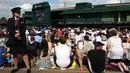 Petugas berjaga dekat ribuan penonton yang menyaksikan laga Andy Murray melawan Milos Raonic pada final tunggal putra  Wimbledon Championships 2016 di The All England Lawn Tennis Club,  Wimbledon, London, (10/7/2016).  (AFP/Justin Tallis)