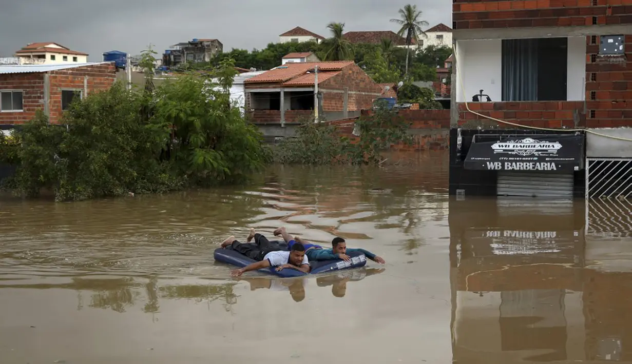 Dua pria menggunakan kasur tiup untuk mengarungi banjir akibat hujan deras di Itapetinga, Negara Bagian Bahia, Brasil, 26 Desember 2021. Gubernur Bahia Rui Costa mengungkapkan pihaknya tengah berupaya membantu proses evakuasi warga terdampak banjir dan mendistribusikan bantuan. (Manuella LUANA/AFP)