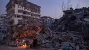 Sejumlah orang beristirahat di dekat api unggun di sekitar gedung-gedung yang runtuh di Hatay, Turki, Senin (13/2/2023). Jumlah korban tewas akibat gempa bumi dahsyat yang melanda Turki dan Suriah meningkat di atas 35.000 pada 13 Februari 2023. (Yasin AKGUL/AFP)