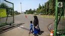 Sejumlah warga berjalan di depan kawasan Monumen Nasional (Monas), Jakarta, Minggu (26/7/2020). Sejumlah warga mulai mengunjungi kawasan Monas meski masih ditutup sementara di masa PSBB transisi. (Liputan6.com/Faizal Fanani)