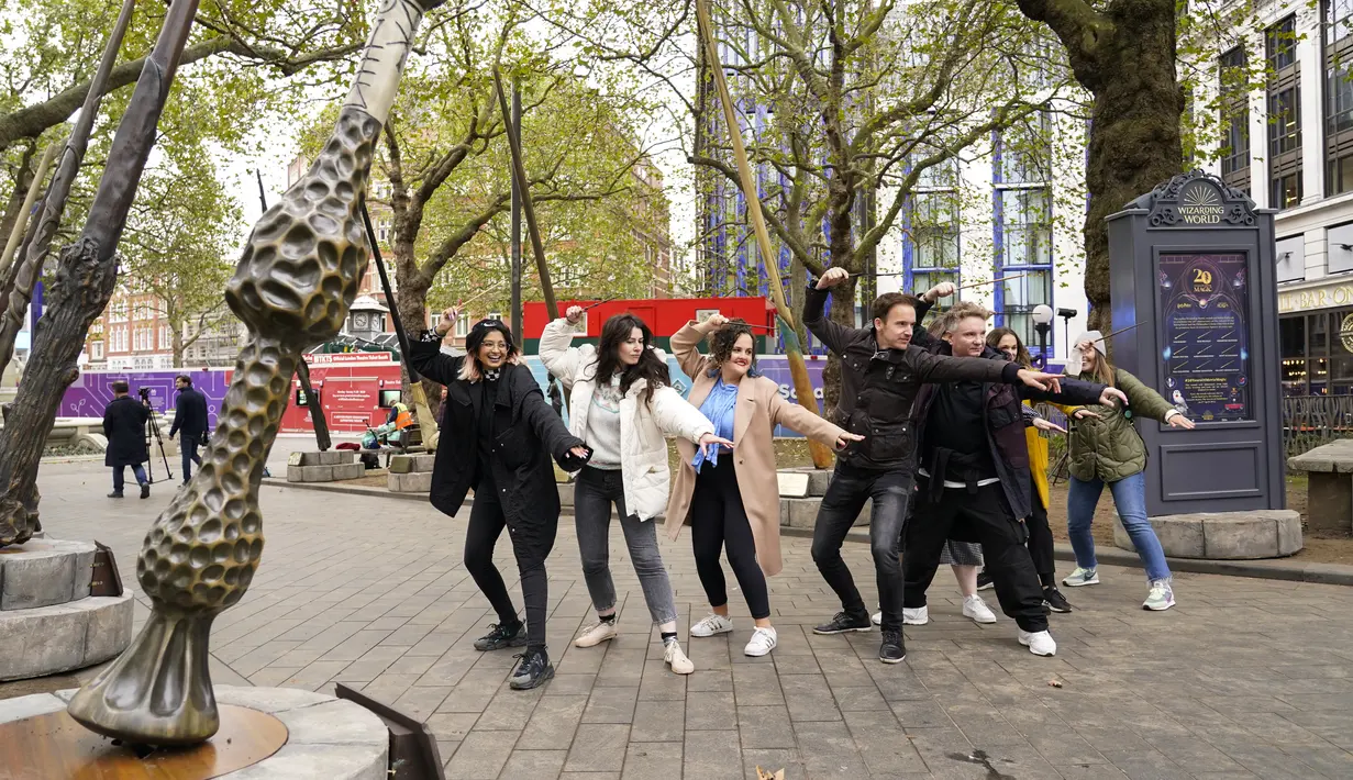 Orang-orang berpose di bawah tongkat raksasa untuk peringatan 20 tahun film Harry Potter and the Philosopher's Stone di Leicester Square, London, Rabu (13/10/2021). Instalasi terdiri dari sembilan tongkat setinggi 15 kaki yang mewakili sembilan karakter kunci dari film. (AP Photo/Alberto Pezzali)