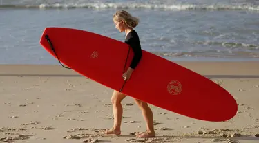 Seorang wanita membawa papan selancar bersiap bermain saat pembatasan sosial Covid-19 mulai dilonggarkan di Pantai Bondi di Sydney, Selasa, (28/4/2020).  Pantai ini terbuka untuk perenang dan peselancar untuk berolahraga saja. (AP Photo/Rick Rycroft)