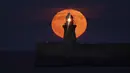 Bulan purnama yang dikenal sebagai Harvest moon muncul di atas mercusuar South Shields di pantai timur laut Inggris, Senin (20/9/2021). Ahli bulan NASA, Gordon Johnston, menerangkan harvest moon adalah bulan purnama yang paling dekat dengan titik balik musim gugur. (Owen Humphreys/PA via AP)