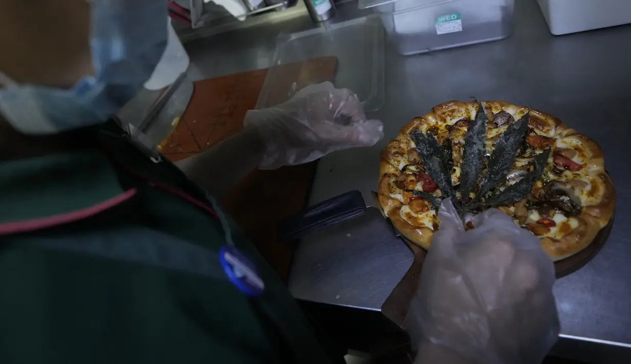 Seorang pekerja menghias pizza dengan daun ganja goreng di sebuah restoran di Bangkok, Thailand  pada 24 November 2021. Pizza bercita rasa sup Tom Yum Gai itu diberi sentuhan daun cannabis yang digoreng kering di atasnya. (AP Photo/Sakchai Lalit)
