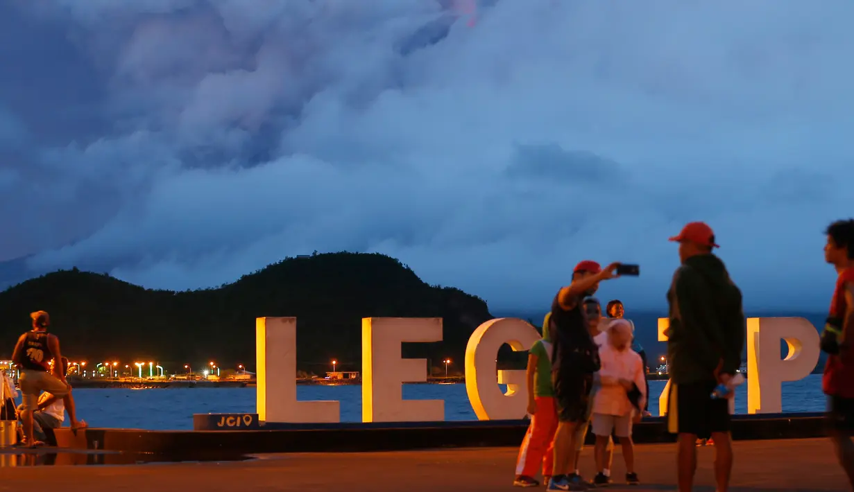 Warga mengambil foto saat Gunung Mayon meletus ringan di Kota Legazpi, Provinsi Albay, tenggara Manila, Filipina, Sabtu (27/1). Meski memesona, letusan lava panas semakin berbahaya. (AP Photo/Bullit Marquez)