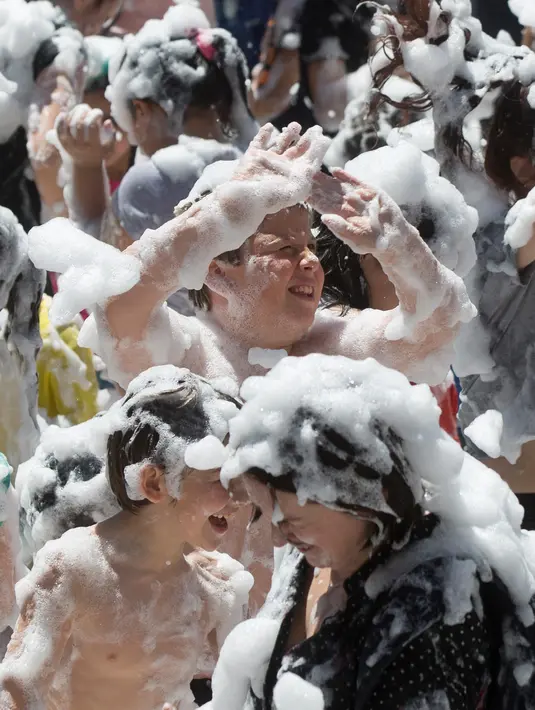 Orang tua dan anak-anak disemprot dengan busa oleh petugas pemadam kebakaran selama pesta di distrik Malasana Madrid, Spanyol, (4/5/2019). (AP Photo/Paul White)