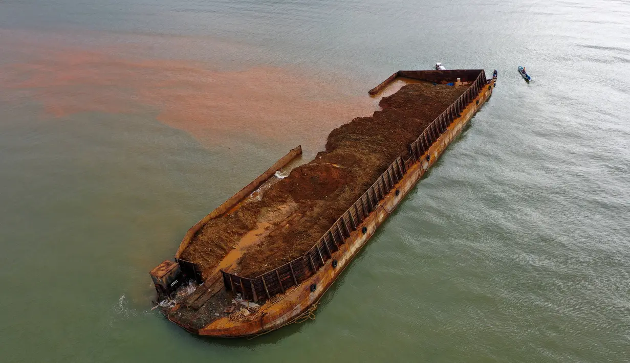Foto udara menunjukkan perahu nelayan berlayar di sekitaran kapal tongkang pengangkut nikel yang karam dan mencemari laut di perairan tujuan wisata Pantai Gong di Konawe, Sulawesi Tenggara (14/7/2021). Hal tersebut terjadi karena diduga tali kapal tongkang putus saat dihantam ombak besar. (AFP/Ono)