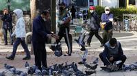 Orang-orang yang memakai masker untuk membantu melindungi dari penyebaran virus corona COVID-19 memberi makan burung merpati di sebuah jalan di Goyang, Korea Selatan, Rabu (11/11/2020). (AP Photo/Ahn Young-joon)